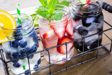 Three mason jars filled with blueberries, strawberries, and black berries, topped with mint.