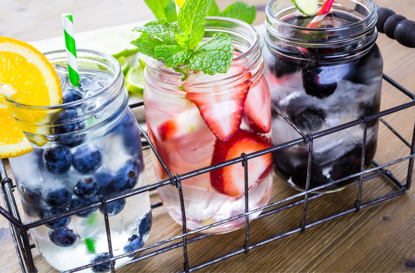 Three mason jars filled with blueberries, strawberries, and black berries, topped with mint.
