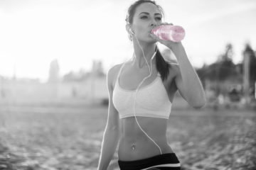 A girl drinks from a berry KSP tabs water bottle on the beach.