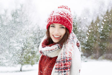 A woman in a red and white coat and hat smiles in the snow.