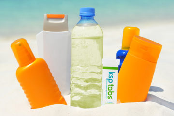 A lime KSP tabs tube sits next to a bottle of water and sunscreen on the beach.