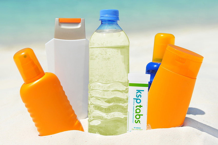 A lime KSP tabs tube sits next to a bottle of water and sunscreen on the beach.