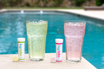 A tube and tablet of Lime KSPtab with a glass of lime KSP by a pool. Also showing the same in berry flavor.