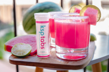A berry KSP tab tube sits next to a glass of watermelon drink.