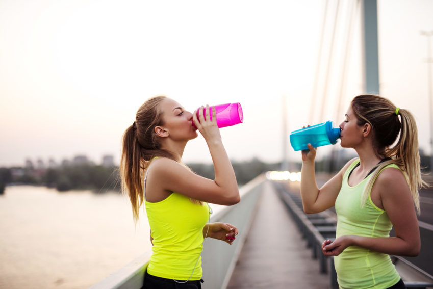 Two girls sipping water bottles on a bridge after a workout.