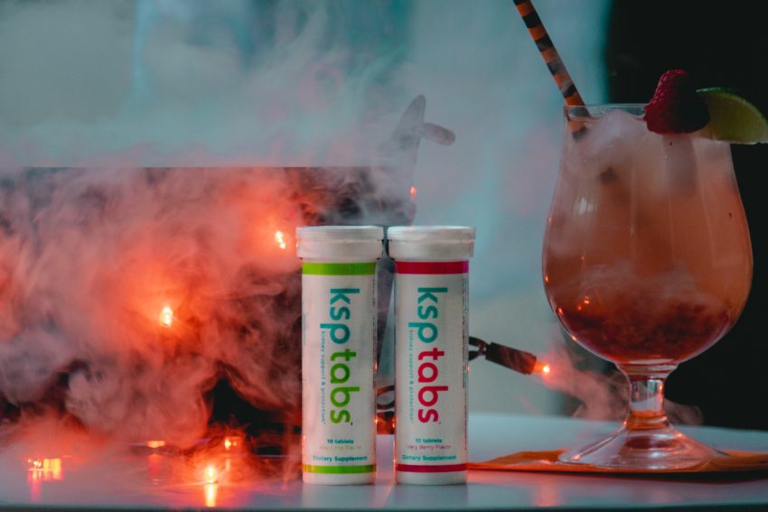 Halloween punch with a tube of lime KSP next to berry KSP. A glass of red punch sits next to them.