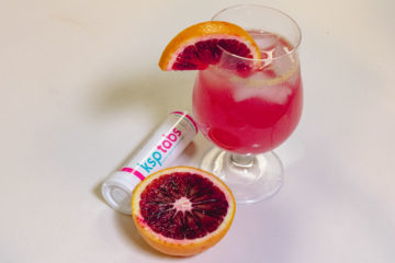 A blood orange cut in half next to a berry KSP tab and a drink made between the two.