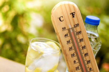 A glass of lemon water next to a thermometer showing that it's hot.