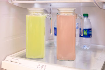 A pitcher of Lime KSP and a pitcher of Berry KSP sits in a refrigerator with plain water bottles behind it.