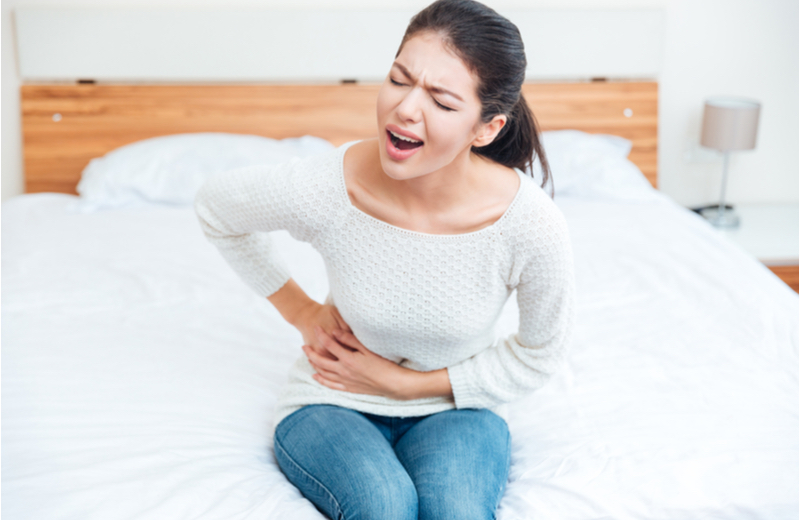A woman sits on the edge of the bed holding her side in pain.